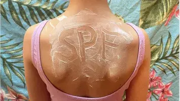Top of a female's back, wearing swimsuit with letters 'SPF' written in sunscreen on skin
