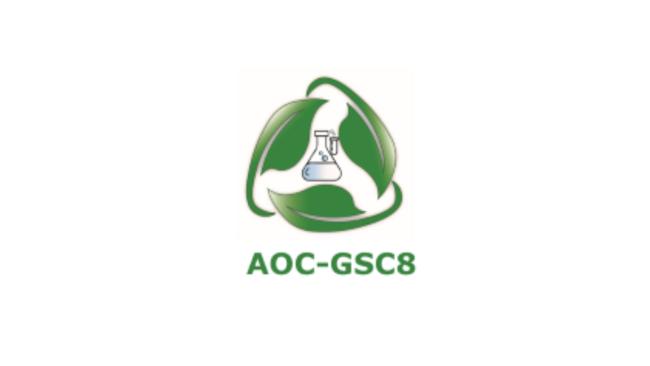 A beaker is centered against a green collection of leaves assembled in a recycling logo shape. The green text reads: AOC-GSCB